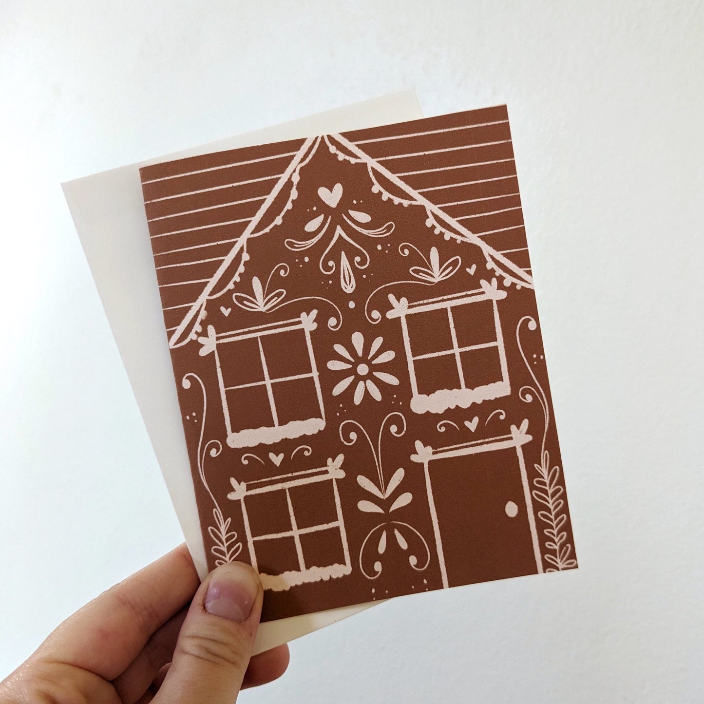 Hand holding a gingerbread house greeting card and a white envelope. 